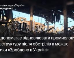 На інформаційному банері з цитатою про урядову допомогу у відновленні промислової інфраструктури в межах політики «Зроблено в Україні» зображено масштабні руйнування всередині виробничого або складського приміщення зі знищеним дахом та купою понівеченого металу після обстрілу