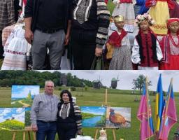 Колаж із двох фотографій показує жінку в чорній вишиванці, яка спочатку позирує поруч із чоловіком на тлі великих ляльок-мотанок, а потім з іншим чоловіком біля виставки картин, столу з прапорами та старовинних вітряків на зеленій галявині.