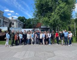 Великий натовп людей стоїть у шеренгу на брукованій площі для спільного фото на тлі міських будівель, високих зелених дерев та вказівників із написом «Дебальцеве» та «Луганськ»