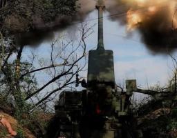 На замаскованій серед дерев бойовій позиції зафіксовано момент потужного пострілу з великої артилерійської системи, коли з її піднятого вгору дула вириваються густі клуби темного диму та яскраве полум'я.