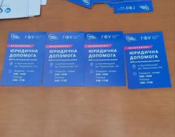 На дерев'яному столі розкладено сині інформаційні картки з текстом «БЕЗОПЛАТНА ЮРИДИЧНА ДОПОМОГА ВПО та постраждалим особам» від організацій «Право на захист» та «ГФУ», де зазначено адресу в місті Кропивницький та графік роботи.