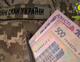 На зображенні видно військову камуфляжну форму з нашивкою «Збройні Сили України», з кишені якої виглядають паперові купюри номіналом 200 та 500 гривень, а у верхньому правому куті розміщено логотип Новоайдарської громади