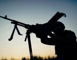 На тлі вечірнього неба знято темний силует українського військового у касці, який цілиться з великокаліберного кулемета, встановленого на станині-тринозі.