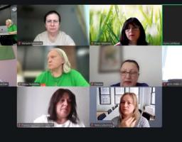 Скриншот екрана показує онлайн-зустріч у Zoom або схожій програмі, де у вікнах сітки розміщені обличчя десятьох учасників, переважно жінок, серед яких один чоловік сидить на тлі прапорів, а інша учасниця транслює відео з групової офлайн-зустрічі в офісі