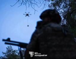 На світлині зображено силует українського військового зі зброєю на передньому плані, який спостерігає за великим гексакоптером у вечірньому небі, що переносить вантаж на тросі, із логотипом 93-ї ОМБр «Холодний Яр» у нижній частині кадру.