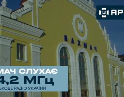 Інформаційний банер військового радіо «Армія FM» показує жовту будівлю залізничного вокзалу міста Бахмач із гербом України та великим текстовим плашками: темно-синьою з логотипом радіостанції у верхньому правому кутку та світло-блакитною з написом «БАХМАЧ СЛУХАЄ 104,2 МГц» у нижній лівій частині