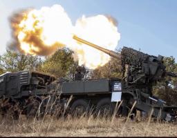 На відкритій місцевості зафіксовано момент потужного пострілу з військової самохідної артилерійської установки на колісному шасі, коли з піднятого вгору дула виривається велика вогняна хмара диму.