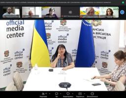 Скриншот онлайн-наради у Zoom або Teams показує трансляцію з офіційного медіацентру Луганської обласної військової адміністрації, де за білим столом на тлі прапорів України та ОВА сидять дві жінки, а у верхній частині екрана видно віконця інших учасників відеодзвінка.