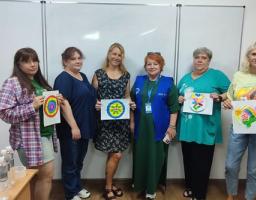 У навчальній аудиторії на тлі великої білої маркерної дошки стоять шість жінок, четверо з яких тримають у руках свої різнокольорові малюнки, створені під час заняття з арттерапії.