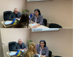 Колаж із двох аналогічних фотографій у робочому кабінеті з бежевими стінами демонструє офіційну зустріч за кутовим дерев'яним столом, де ліворуч сидить сивочолий чоловік в окулярах та сірому піджаку біля маленького прапора України, праворуч — темнокоса жінка в окулярах та рябому чорно-білому жакеті, а на передньому плані спиною до кадру сидить відвідувачка, яка на верхньому знімку має розпущене довге волосся, а на нижньому — зібране у хвіст